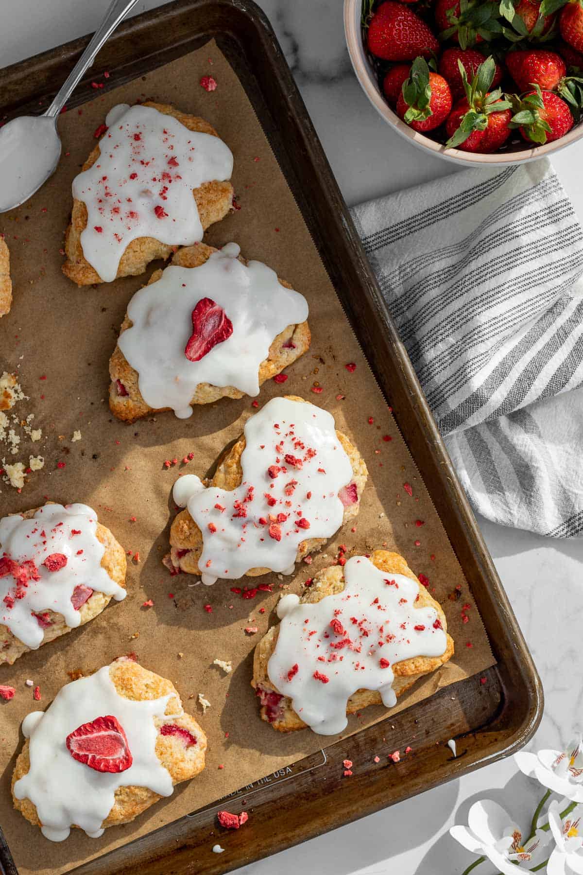 strawberry and cream scones with a vanilla glaze on a baking sheet with a bowl of strawberries next to it