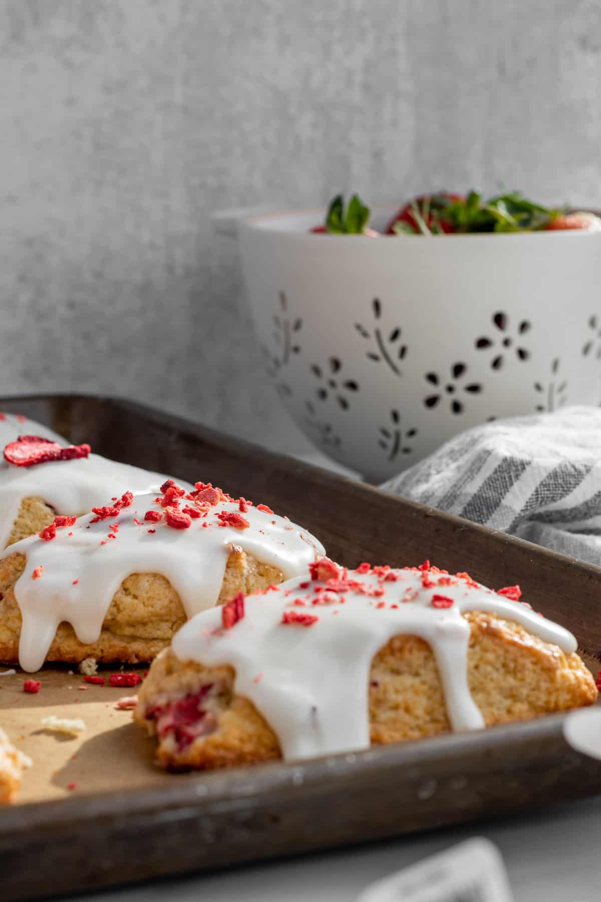 strawberry and cream scones on a baking sheet with a colander of strawberries in the background