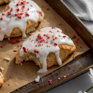 strawberry and cream scones on a baking sheet lined with parchment with a bite out of one scone