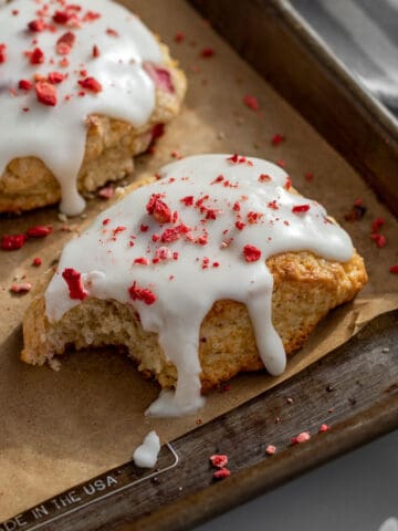 strawberry and cream scones on a baking sheet lined with parchment with a bite out of one scone