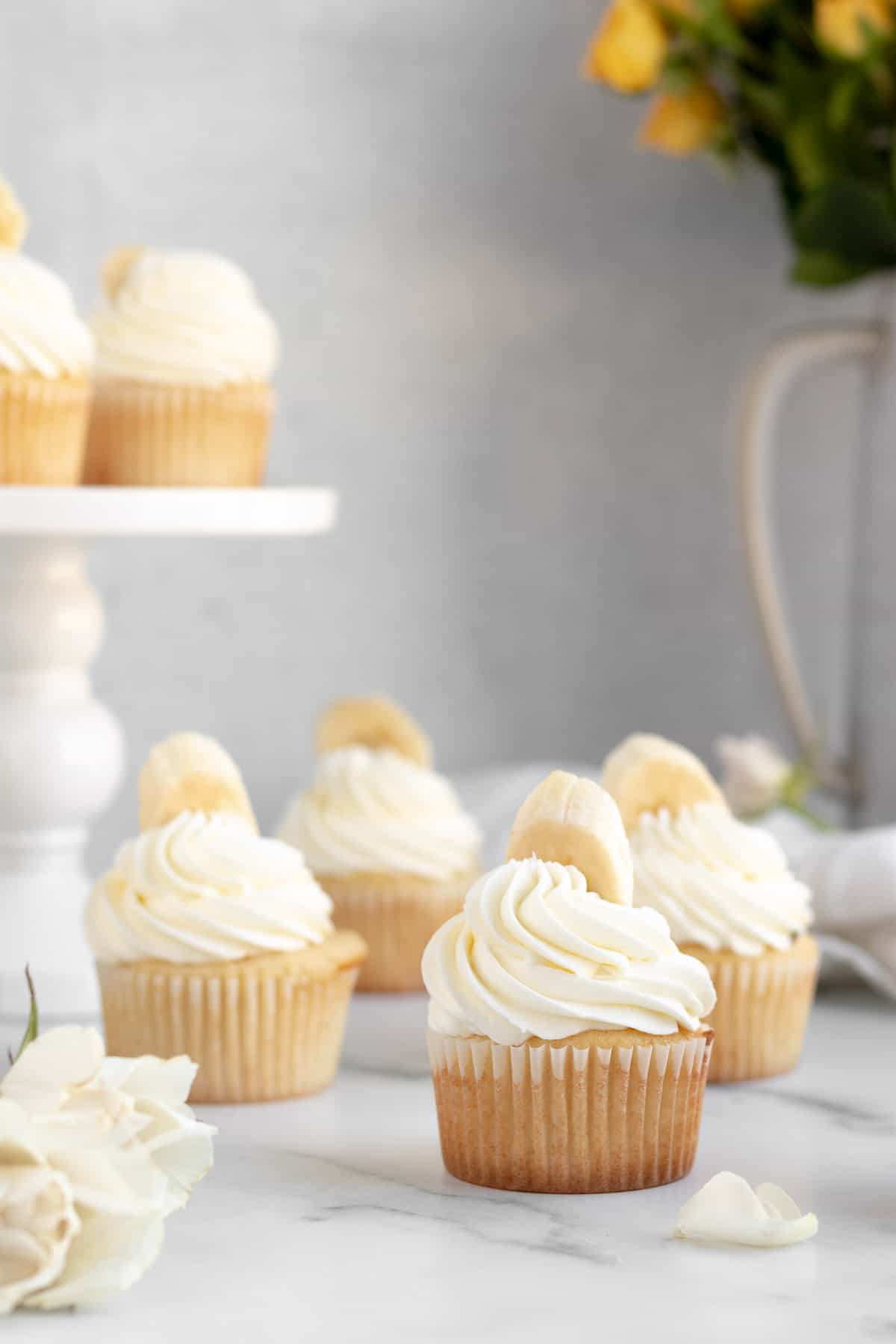 banana pudding cupcakes with white frosting and a banana on top sitting on a marble counter