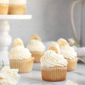banana pudding cupcakes with white frosting and a banana on top sitting on a marble counter
