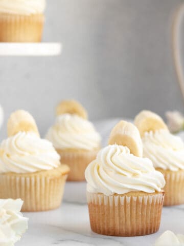 banana pudding cupcakes with white frosting and a banana on top sitting on a marble counter