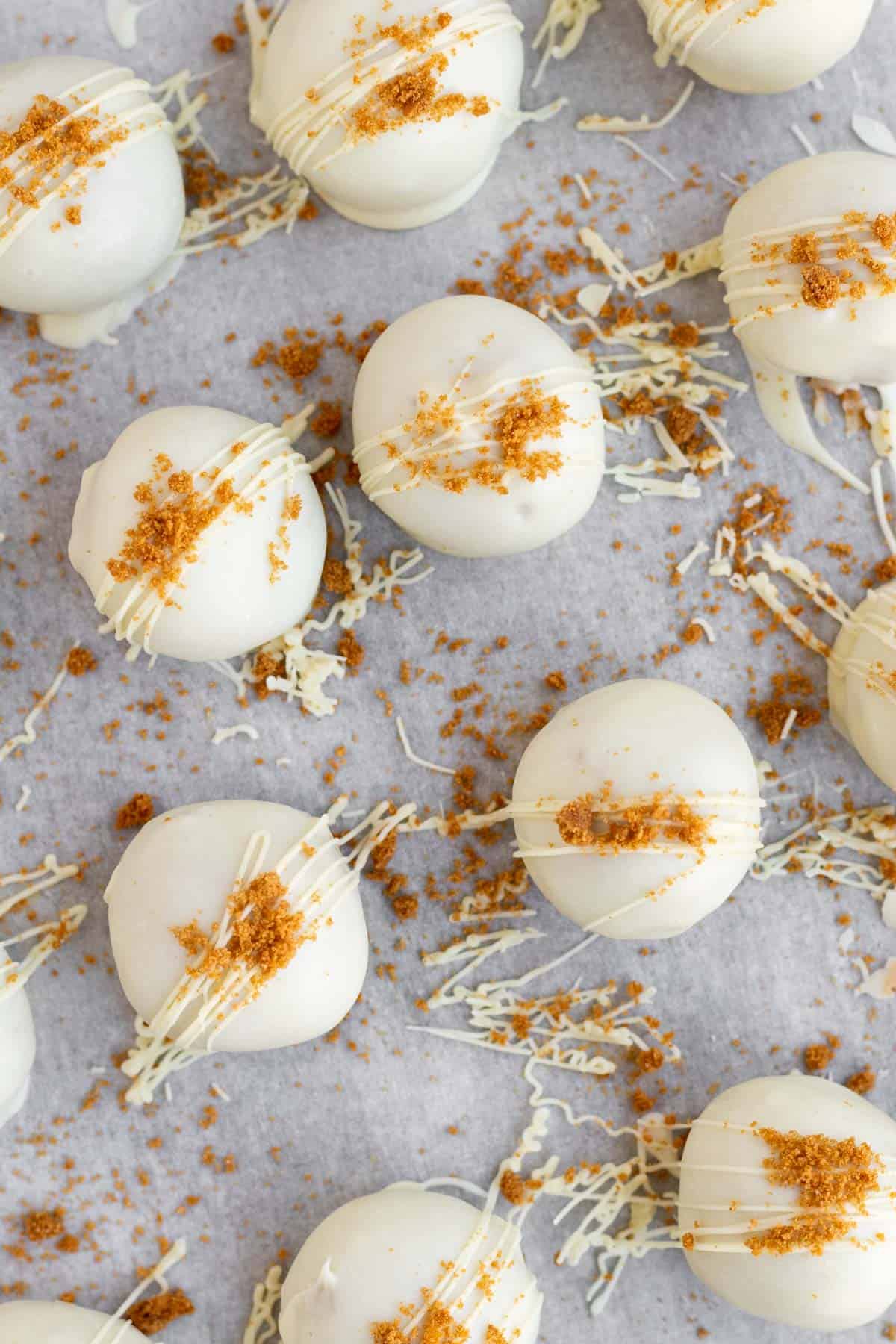 biscoff truffles covered in white chocolate and Biscoff crumbs on a parchment lined baking sheet