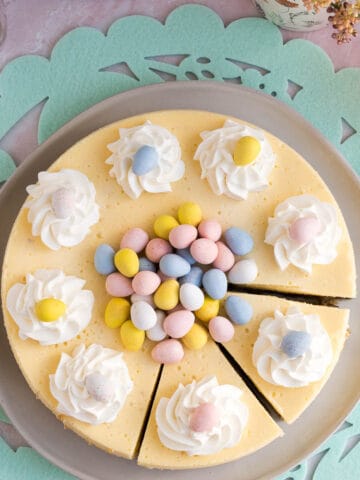 Top view of an Easter egg cheesecake with whipped cream and mini eggs piled on top and 2 slices cut sitting on a green Easter placemat