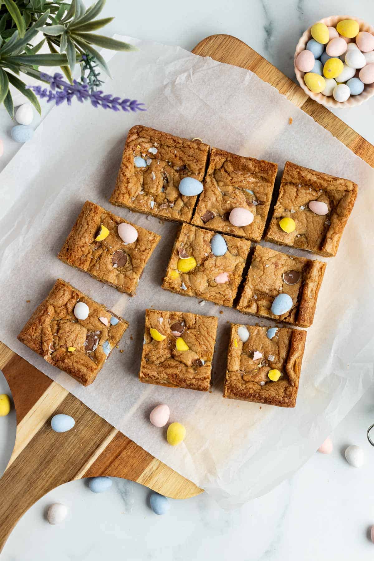 mini egg cookie bars cut into squares sitting on a cutting board with parchment paper on top