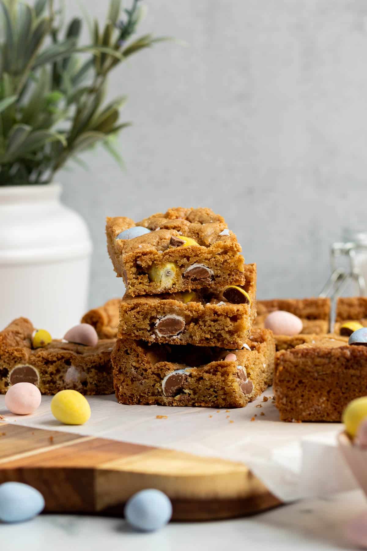 a stack of 3 mini egg cookie bars with a white vase of flowers in the background