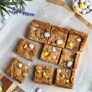 mini egg cookie bars cut into squares sitting on a cutting board with parchment paper on top