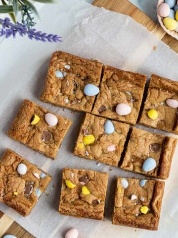 mini egg cookie bars cut into squares sitting on a cutting board with parchment paper on top