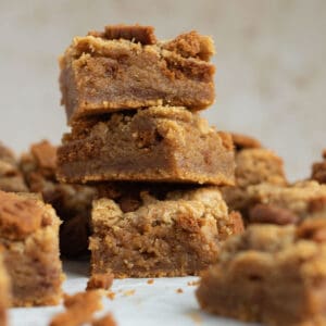 a stack of 3 biscoff blondies with other blondies scattered around them