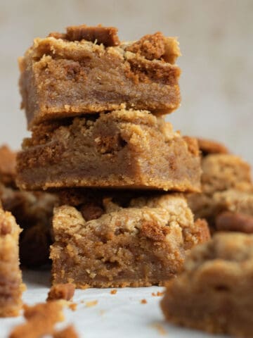 a stack of 3 biscoff blondies with other blondies scattered around them