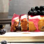 Blackberry lemon bread on a wood cutting board, with 2 slices cut and blackberries piled on top