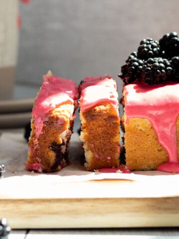 Blackberry lemon bread on a wood cutting board, with 2 slices cut and blackberries piled on top