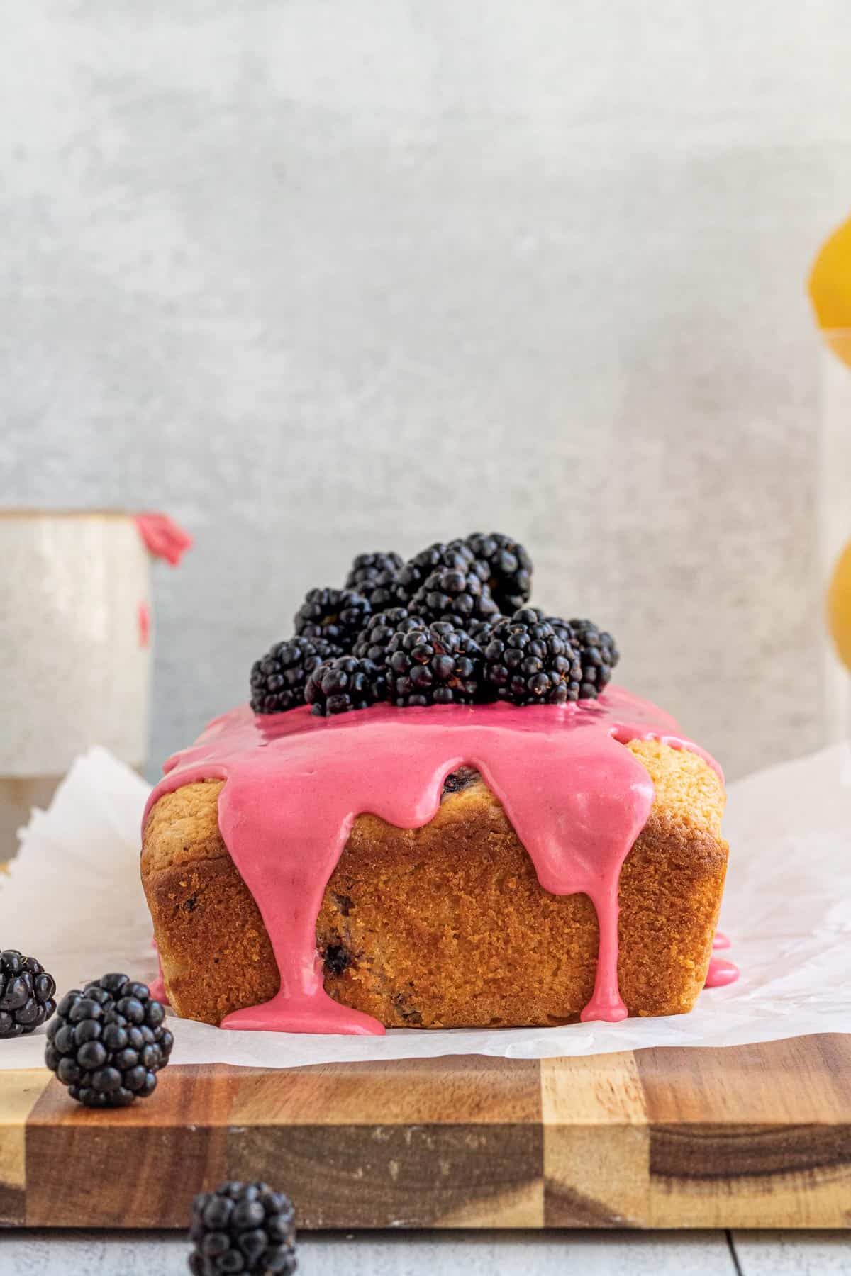 blackberry lemon bread with a pink glaze and blackberries on top sitting on a parchment covered wood board