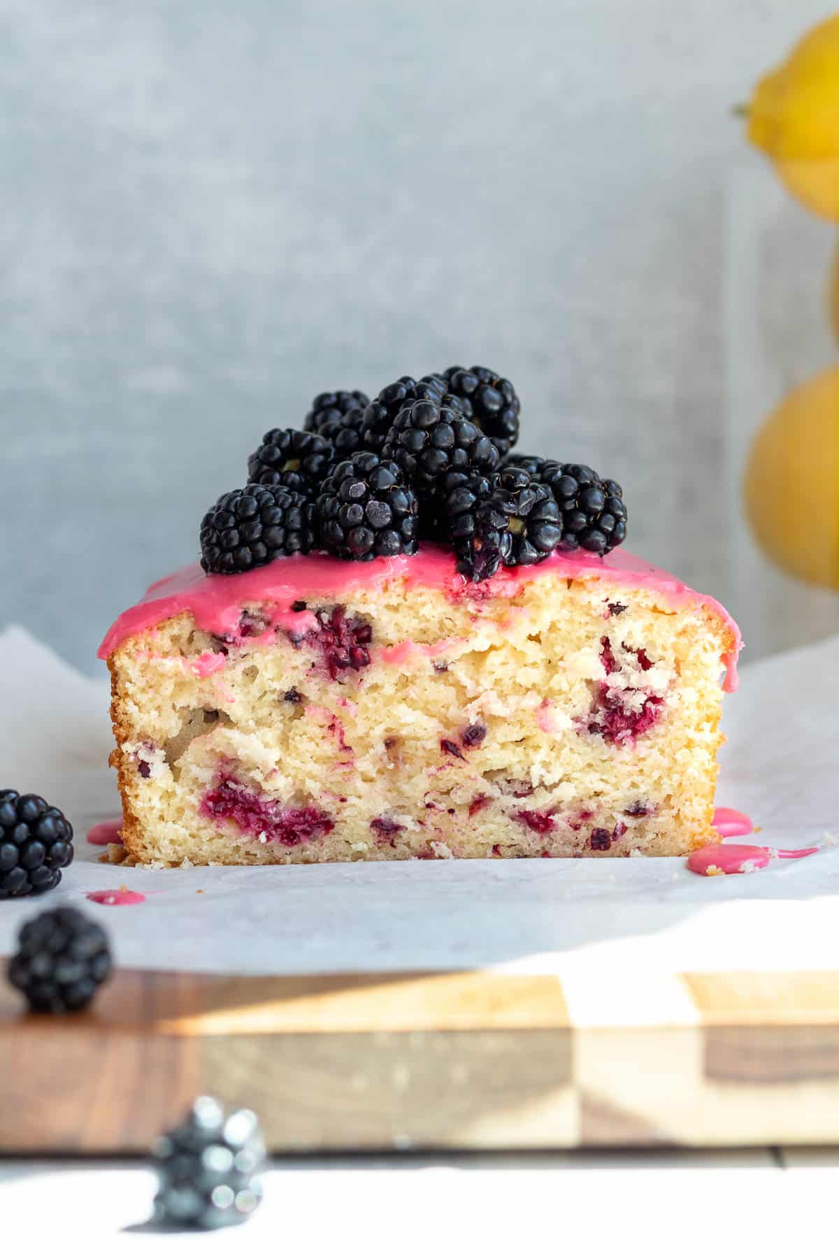 blackberry lemon bread with blackberries piled on top, sliced open and sitting on a wooden cutting board