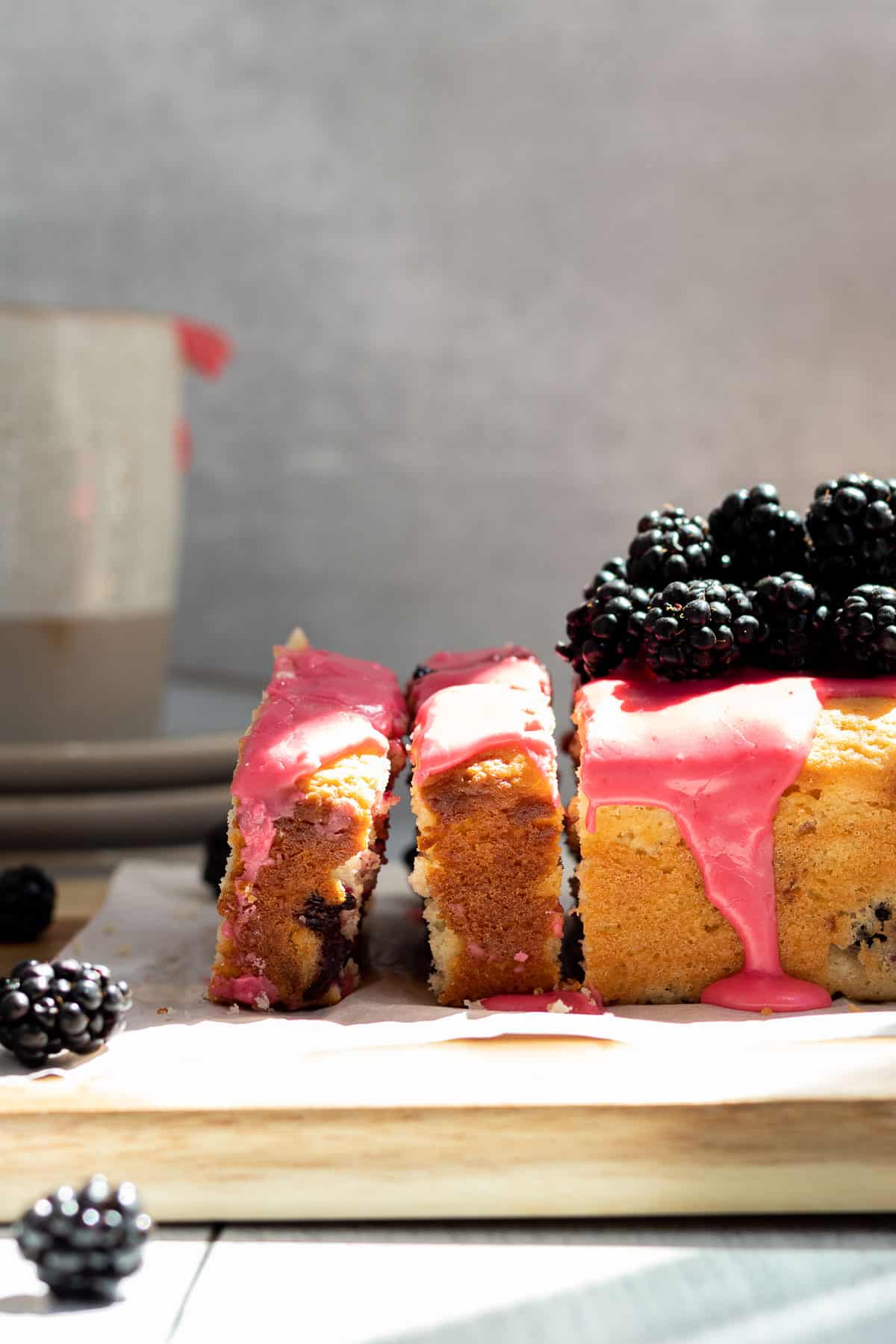 Blackberry lemon bread on a wood cutting board, with 2 slices cut and blackberries piled on top