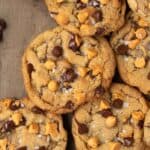 a pile of chocolate chip butterscotch cookies on a cookie sheet with a bowl of chocolate chips and butterscotch chips nearby