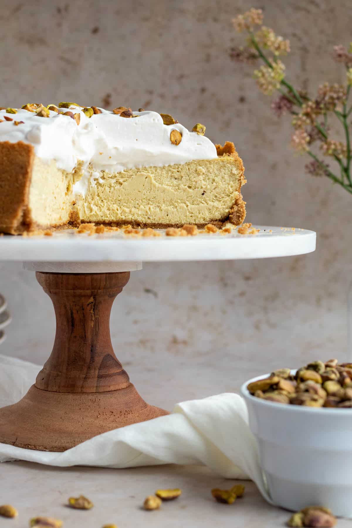 pistachio cheesecake on a wood and marble cake stand with a bowl of pistachios next to it