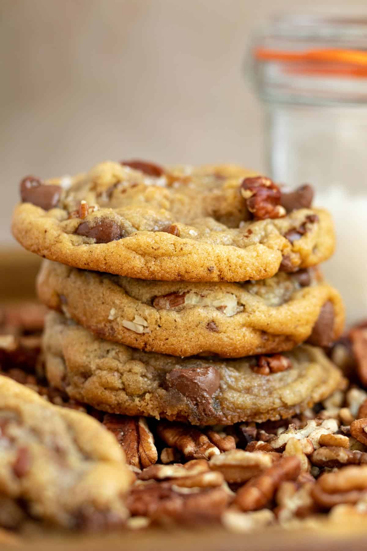 a stack of pecan chocolate chip cookies with a glass container of sea salt in the background