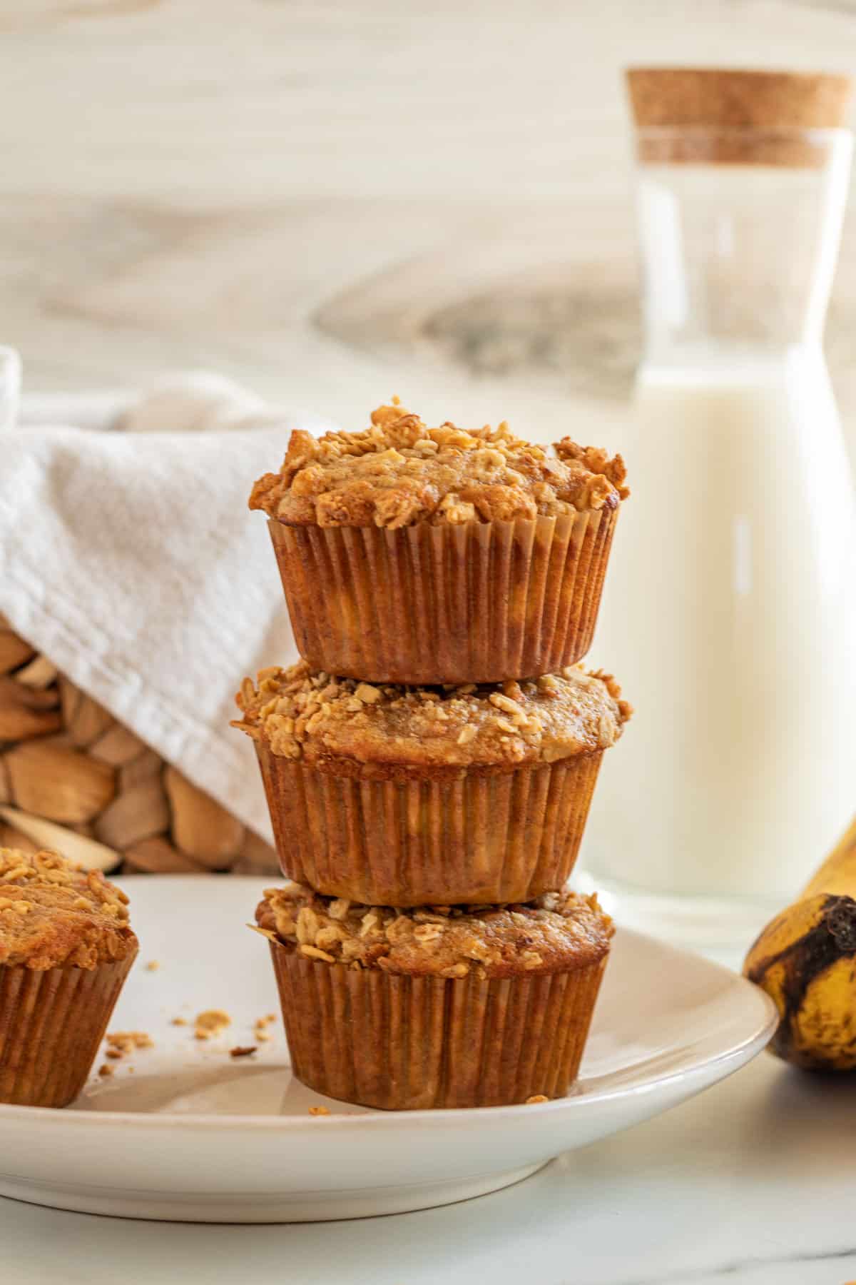 a stack of 3 banana carrot muffins with a pitcher of milk in the background