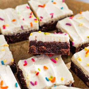 sliced brownies with cream cheese frosting and colored sprinkles sitting on brown parchment paper