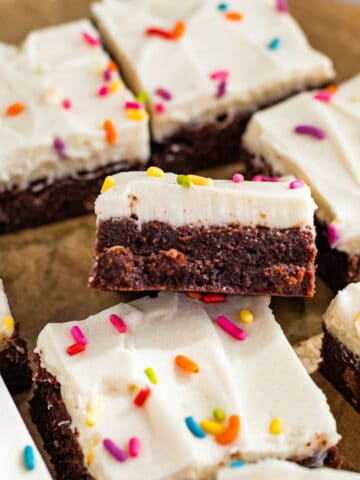 sliced brownies with cream cheese frosting and colored sprinkles sitting on brown parchment paper