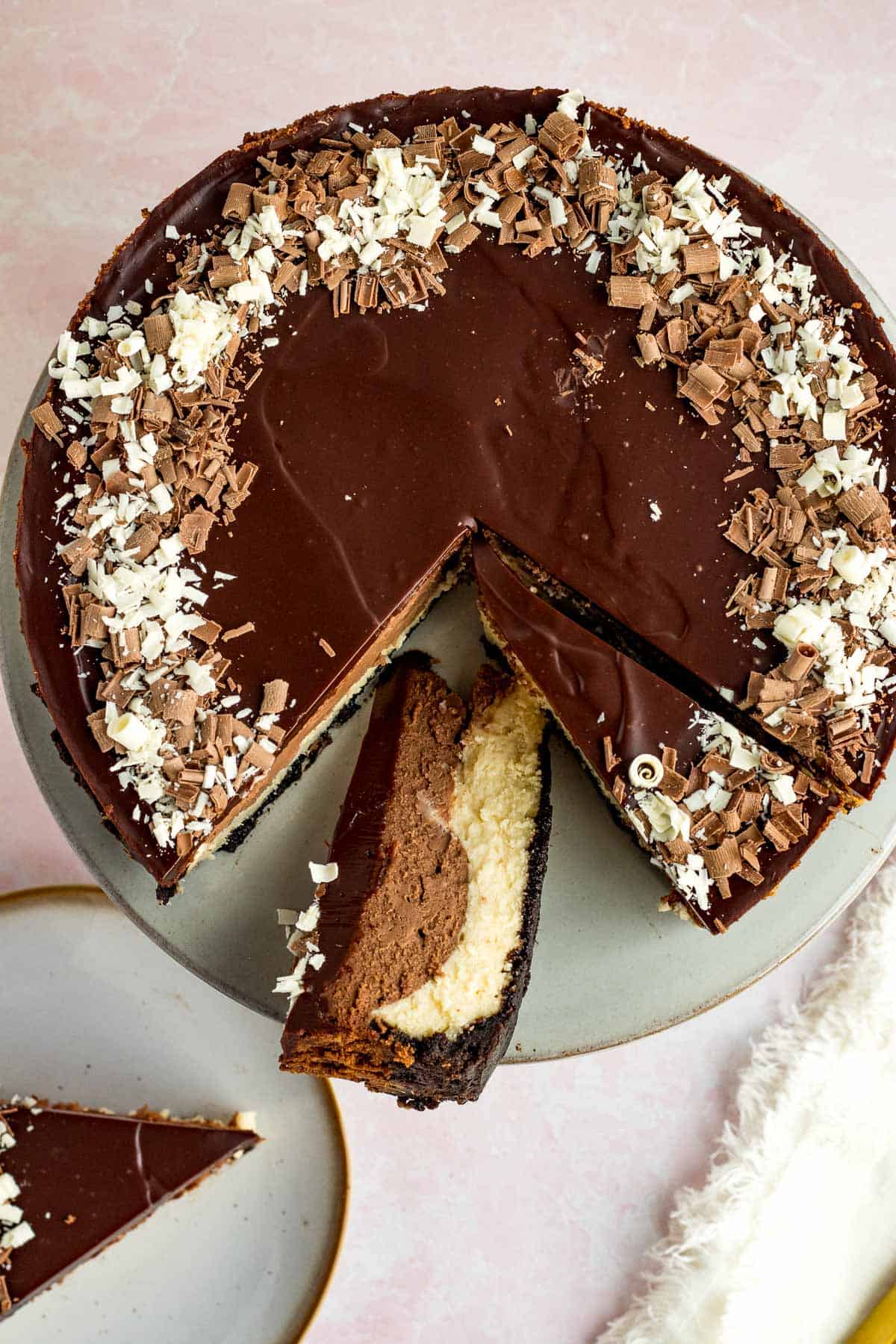 tuxedo cheesecake with chocolate ganache and chocolate shavings on a cake stand with some slices cut out