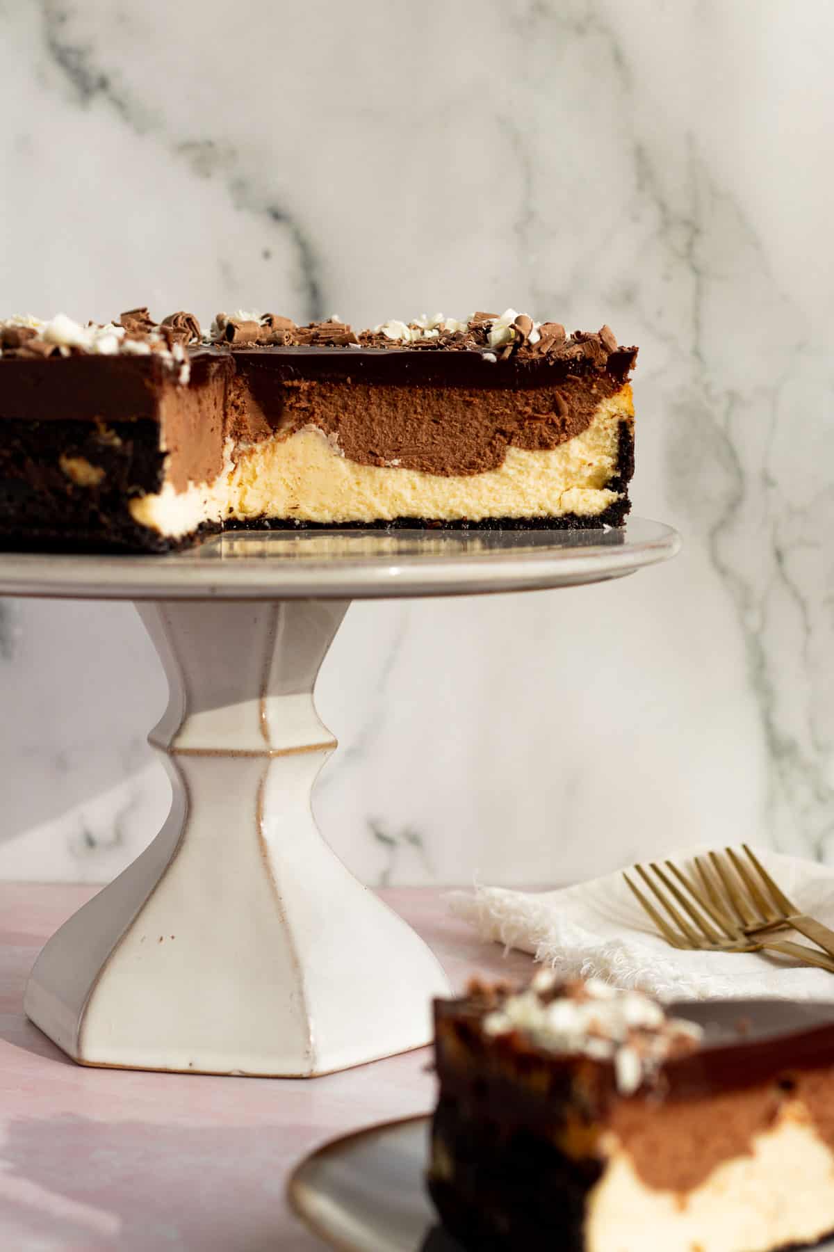 tuxedo cheesecake with layers of chocolate and white chocolate cheesecake on a gray cake stand against a marble background