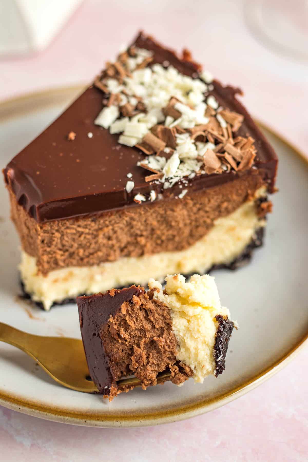 a slice of a tuxedo cheesecake on a plate with one bite on a gold fork 