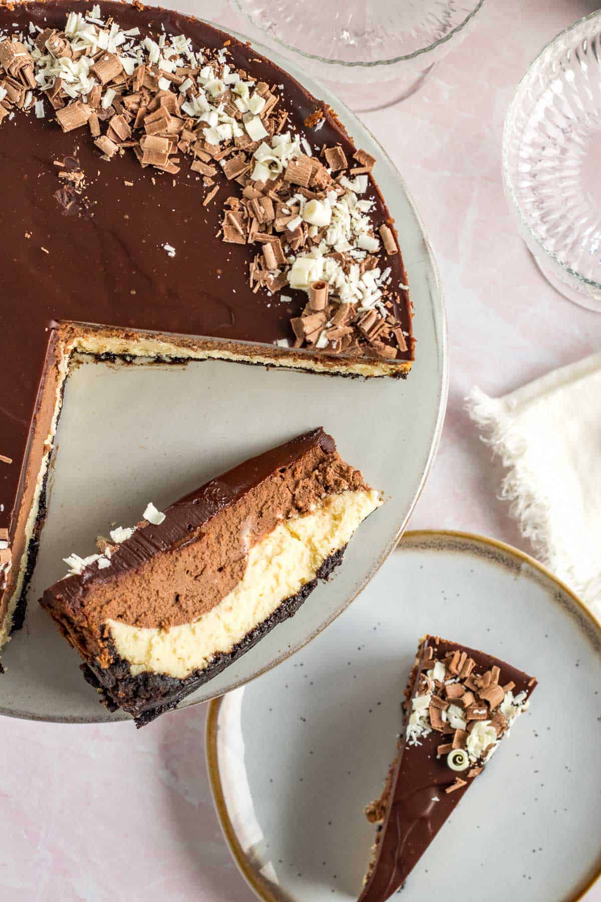 tuxedo cheesecake on a gray cake stand with one slice on a gray plate and one slice on its side on the  cake stand
