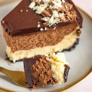 a slice of a tuxedo cheesecake on a plate with one bite on a gold fork