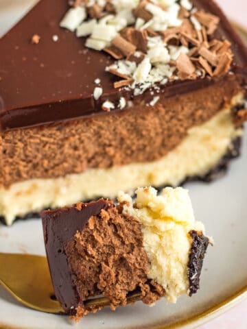 a slice of a tuxedo cheesecake on a plate with one bite on a gold fork