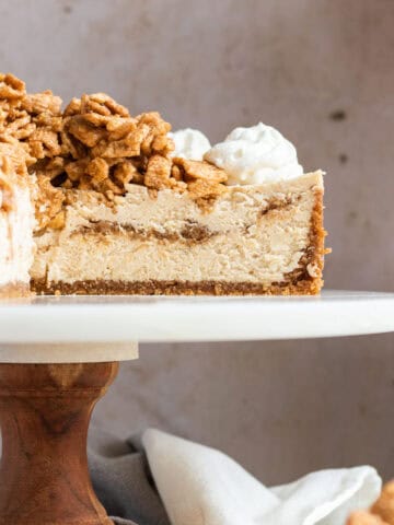 cinnamon toast crunch cheesecake on a wood and marble cake stand with slices cut out to show the inside of the cheesecake