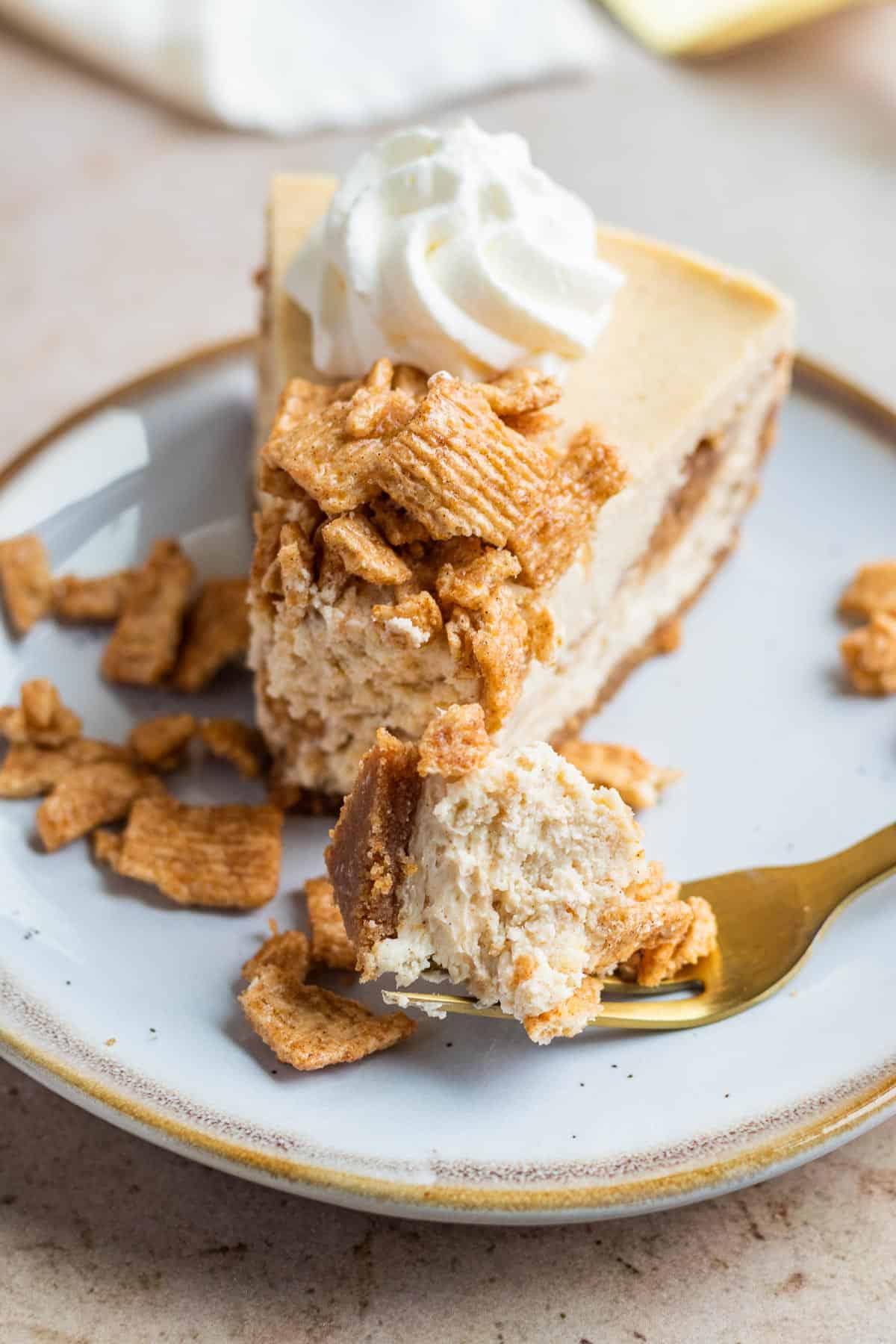 A slice of cinnamon toast crunch cheesecake on a plate with a bite on a gold fork
