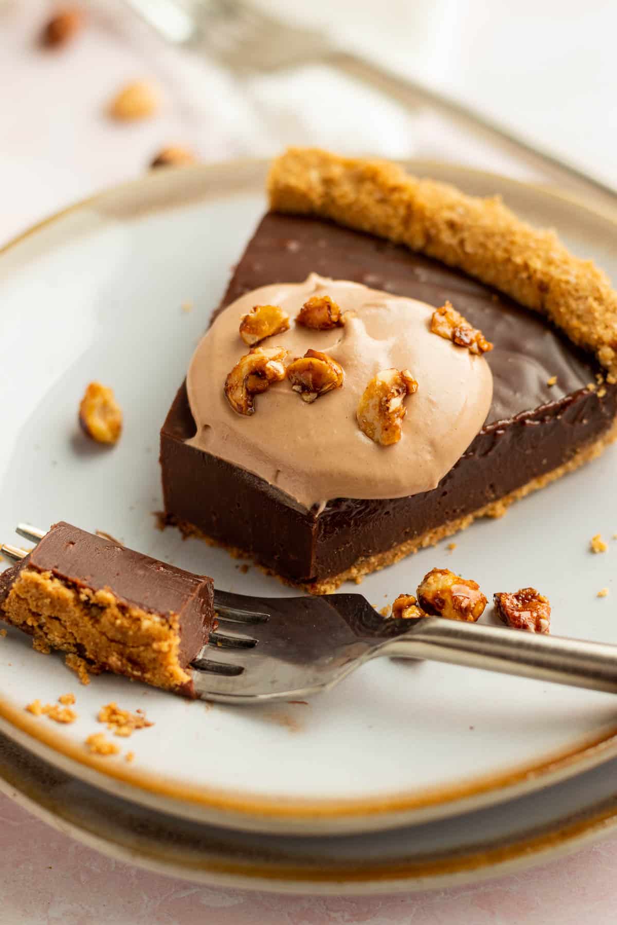 a slice of a nutella tart with nutella whipped cream on a white plate  with a bite on a fork 