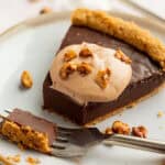 a slice of a nutella tart with nutella whipped cream on a white plate with a bite on a fork