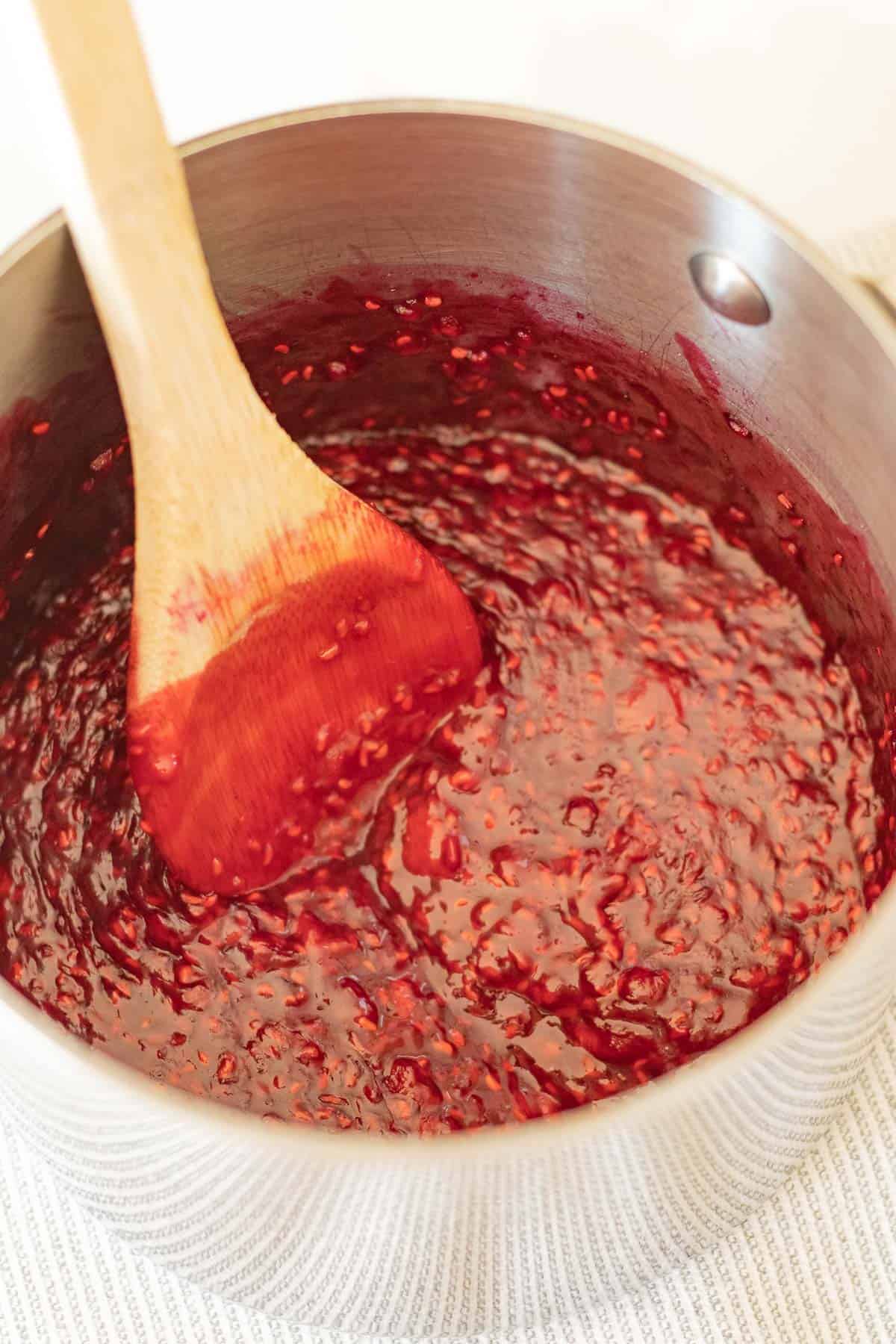 wooden spoon stirring raspberry sauce cooked down in a stainless steel saucepan